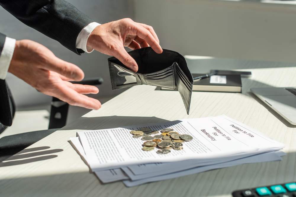 Image of a cropped view of a businessman holding an empty wallet near coins on a petition, featuring 411 Business Law and highlighting 'Steps in Filing for Bankruptcy,' ensuring it aligns with the page's context.