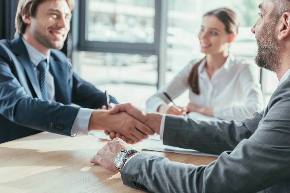 Business people shaking hands during a meeting in a modern office, featuring 411 Business Law, highlighting different types of contracts and aligning with the page's context.